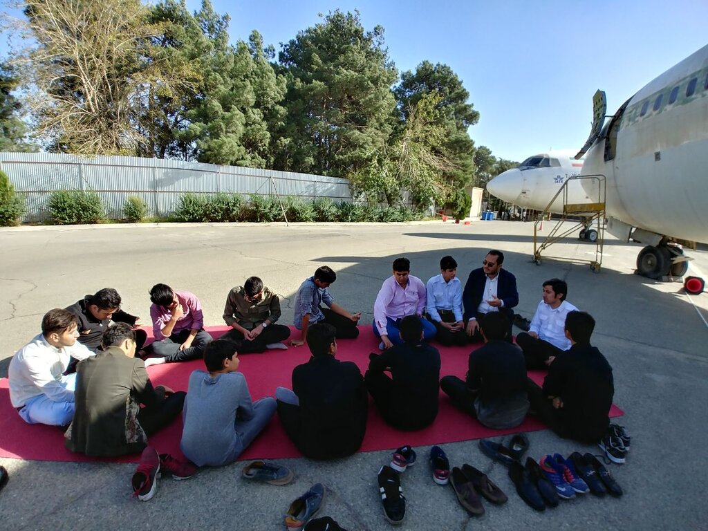 دورهمی هنرجویان در ساعت غیردرسی در حیاط مدرسه که کنار هواپیما برگزار می‌شود